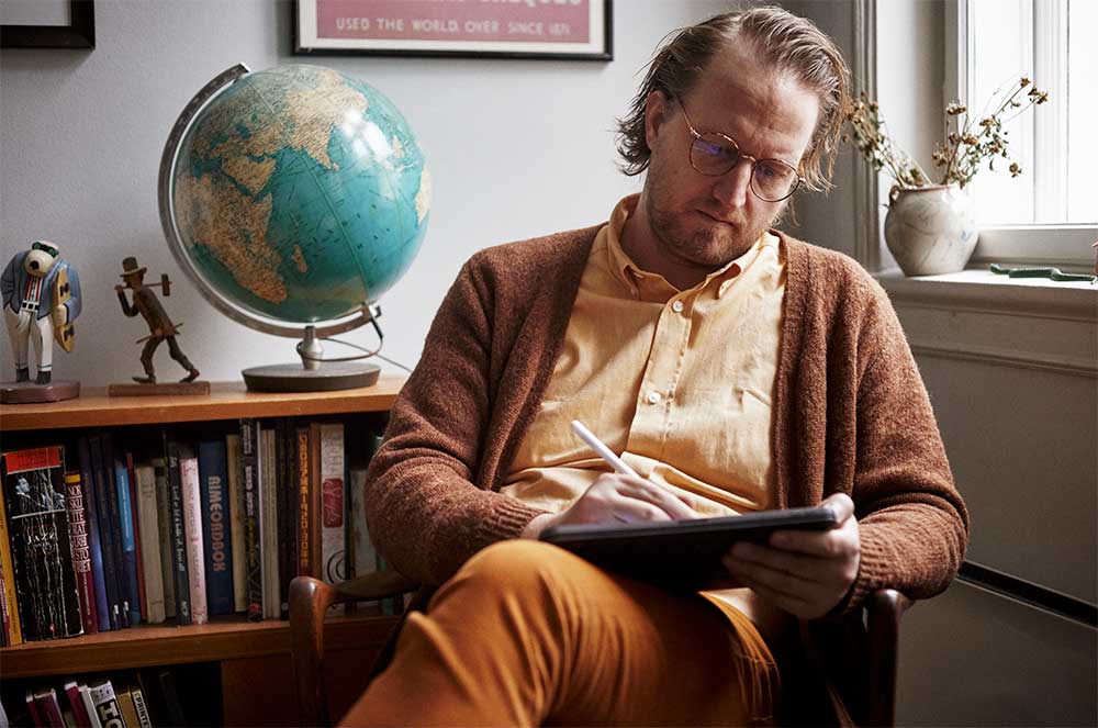 Bendik Kaltenborn working on a tablet in his cozy study, surrounded by books and a globe. Photographed by Lars Petter Pettersen.