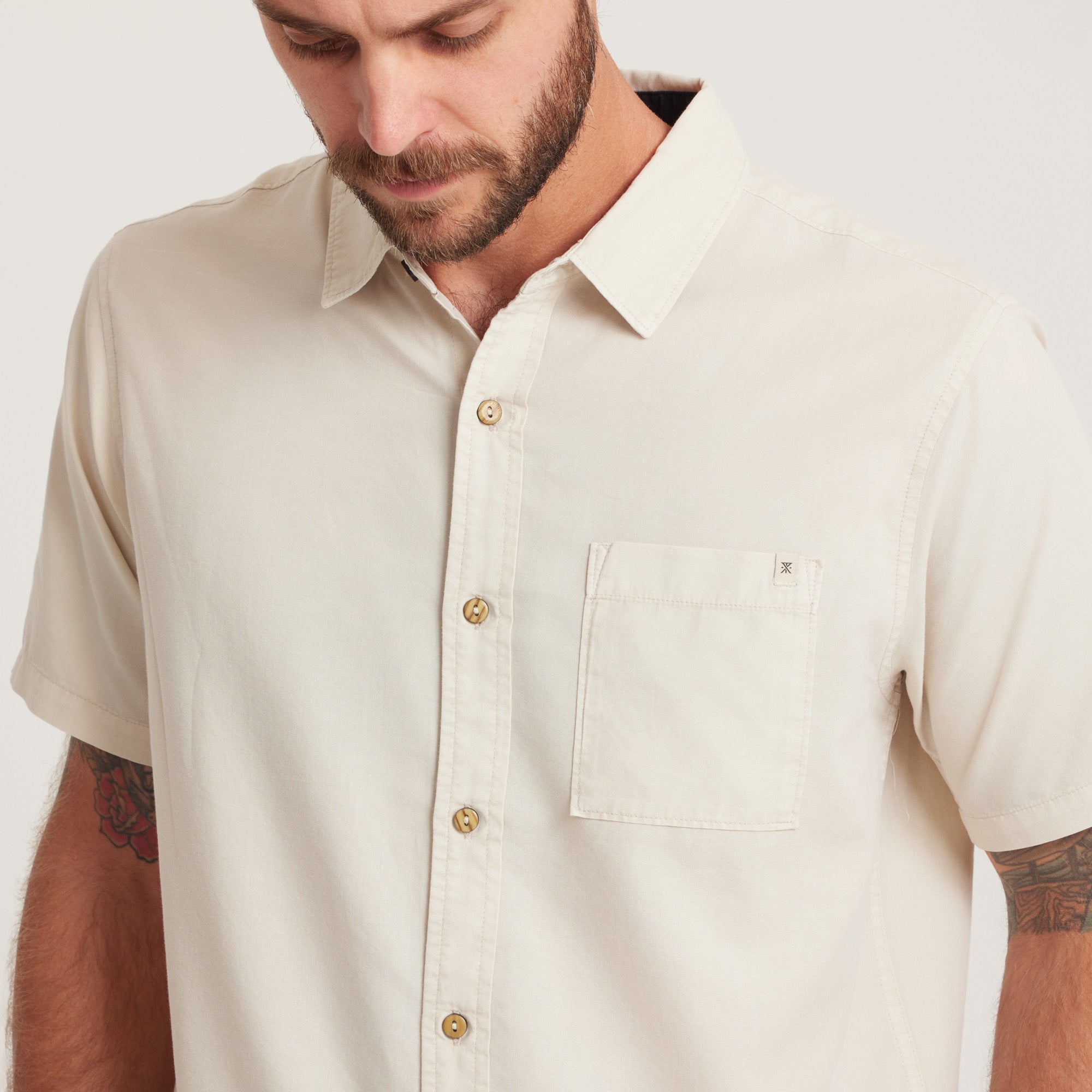 Close-up of a men's short-sleeve button-down shirt in off-white, featuring a chest pocket and natural buttons for a clean, minimalist look.